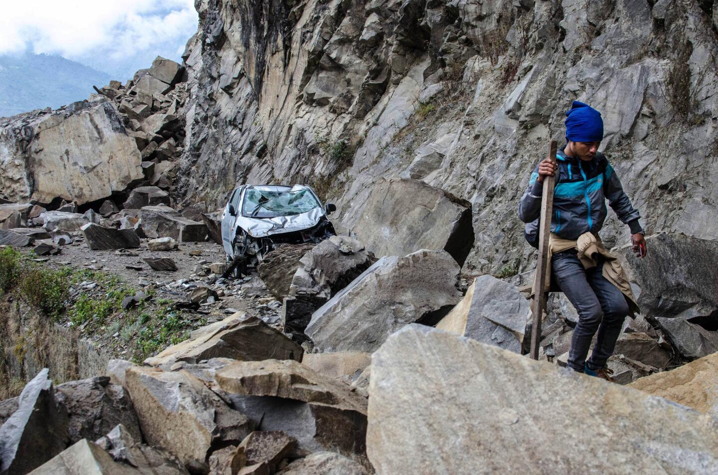 A Nepalese man walks over fallen rocks and past a crushed car on the way to a village in Langtang National Park.