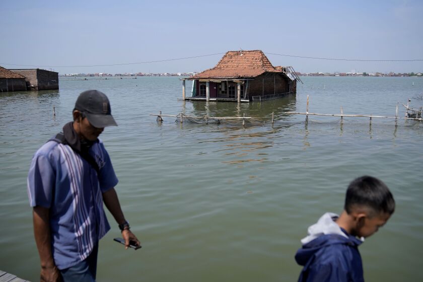 People walk on a path near abandoned homes in Timbulsloko, Central Java, Indonesia, Sunday, July 31, 2022. Scientists say parts of the island will be entirely lost to the sea in the coming years. (AP Photo/Dita Alangkara)