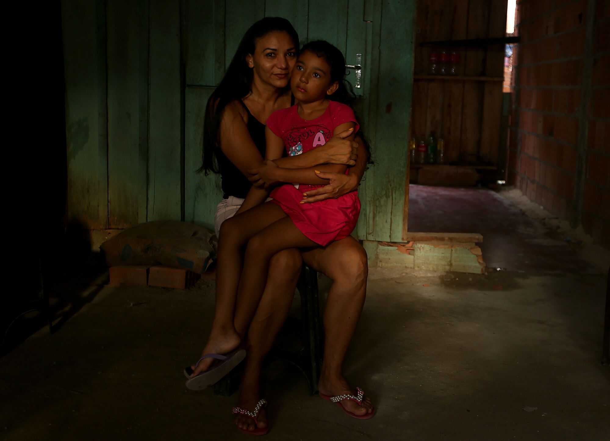 Ludernilce Peixoto Costa and her daughter Adrielly sit in a chair at their home