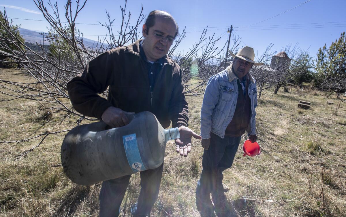 Cuauhtemoc Saenz-Romero, left, and Francisco Ramirez Cruz check out an empty water container on Cruz's ranch in La Mesa, Mexico.