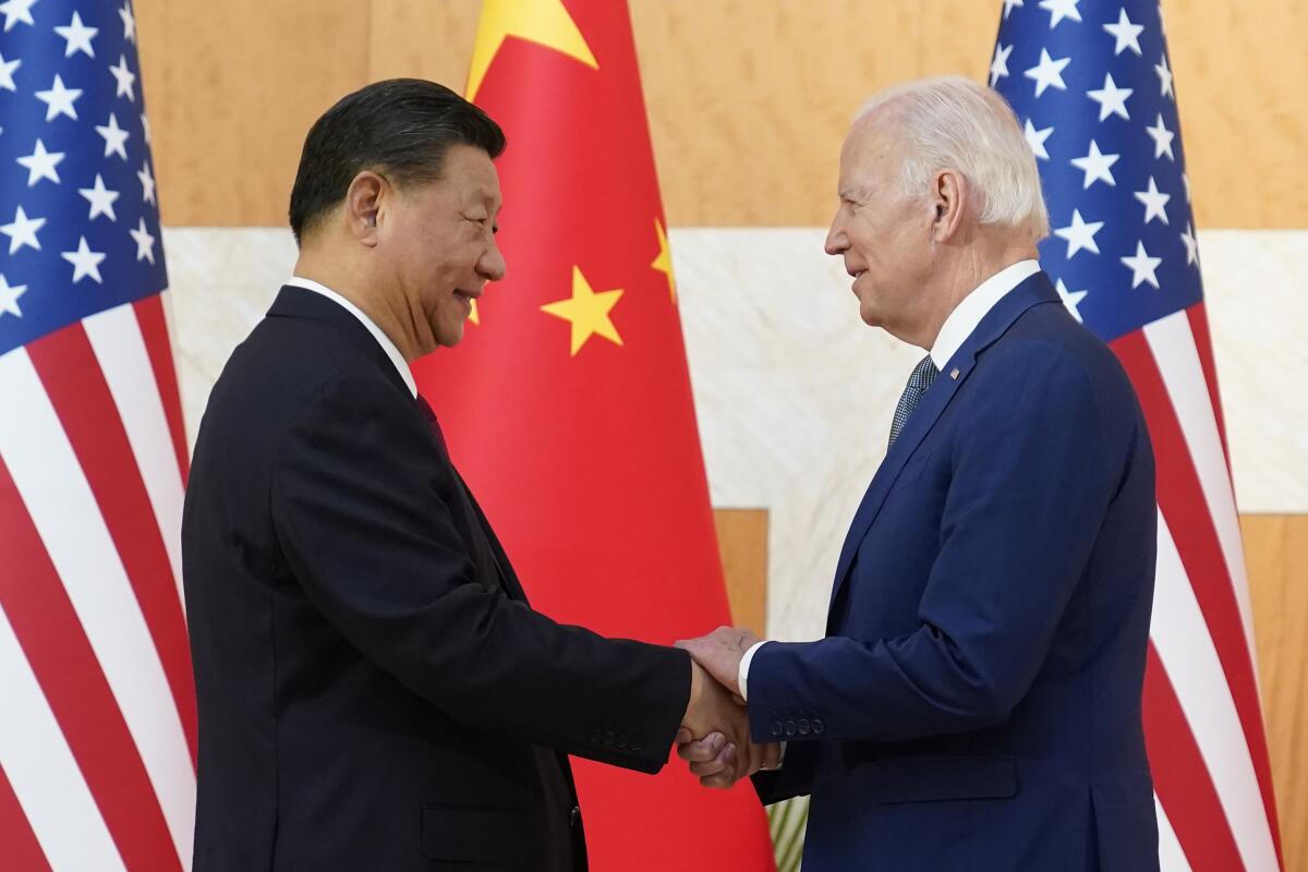 President Biden and Chinese President Xi Jinping shake hands in front of the flags of their countries.