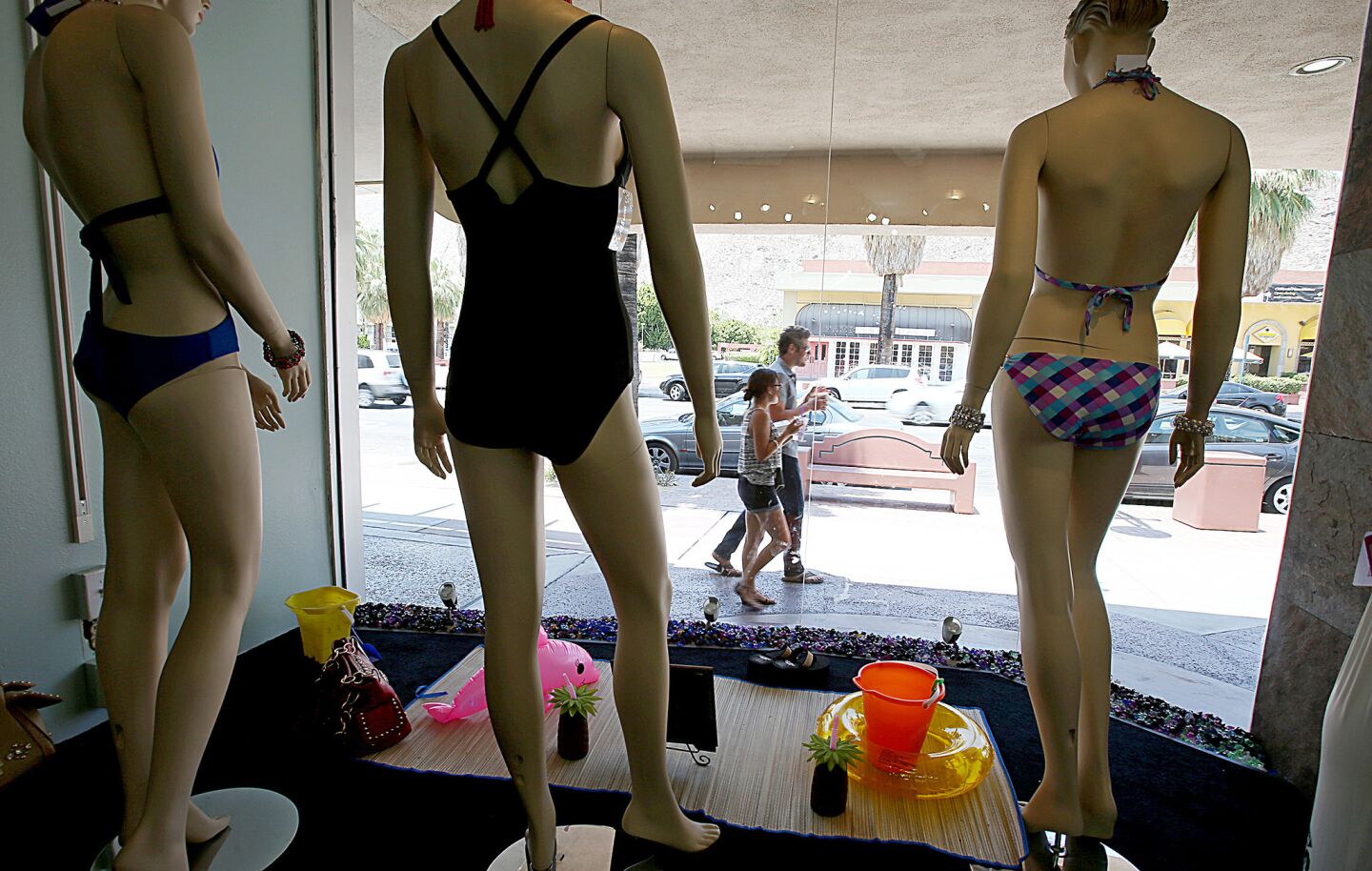 Pedestrians with cold drinks stroll past a window display of bathing suits at the Looksy Couture Boutique in Palm Springs.