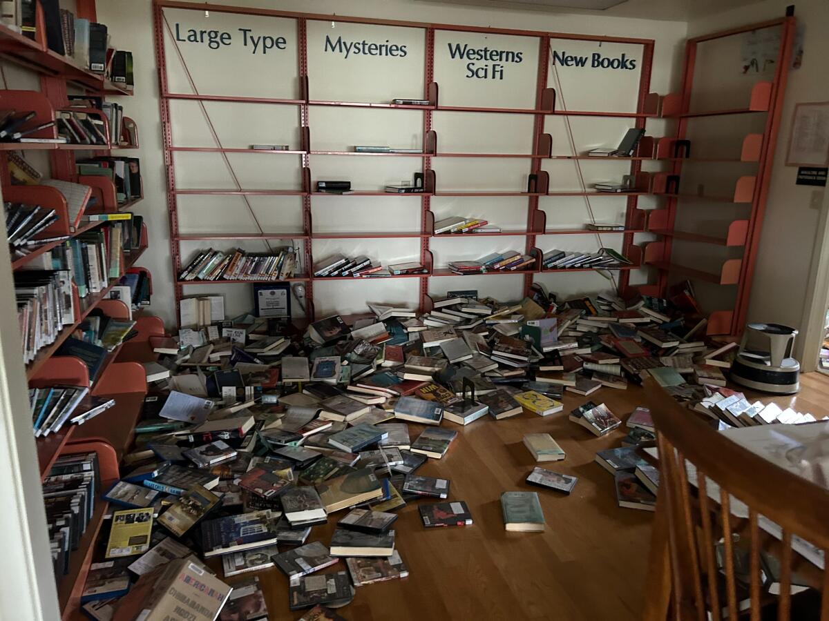 AA view of a room lined with  near-empty bookshelves and books strewn all round on the floor. 