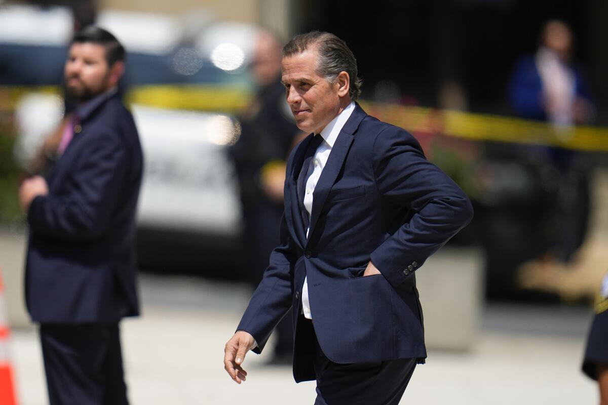 Hunter Biden walking and reaching into his suit jacket pocket against a blurry background