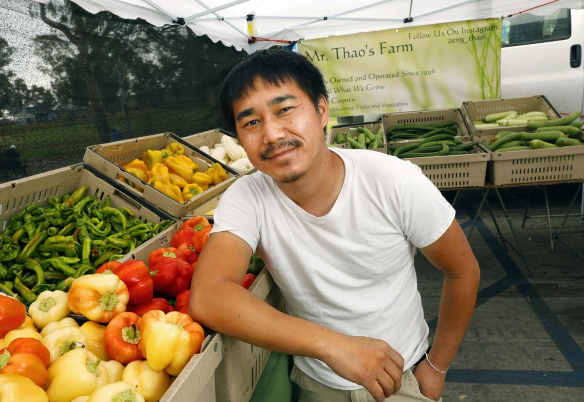 A man stands next to crates of vegetables at a famers market. 