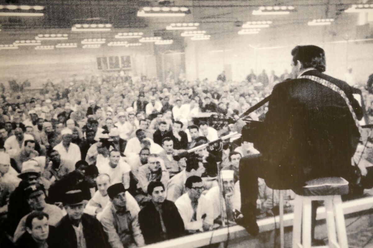 a photograph of a man playing the guitar in front of a crowd of male inmates 