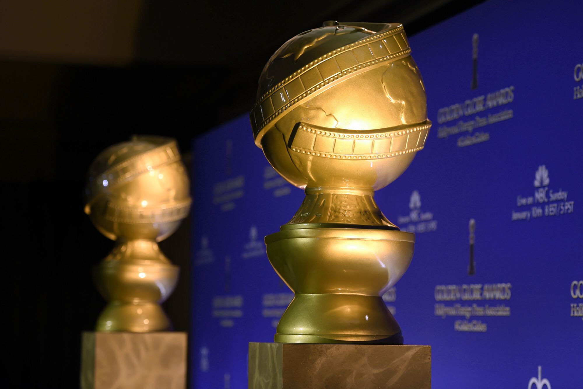 Replicas of Golden Globe statuettes against a blue backdrop