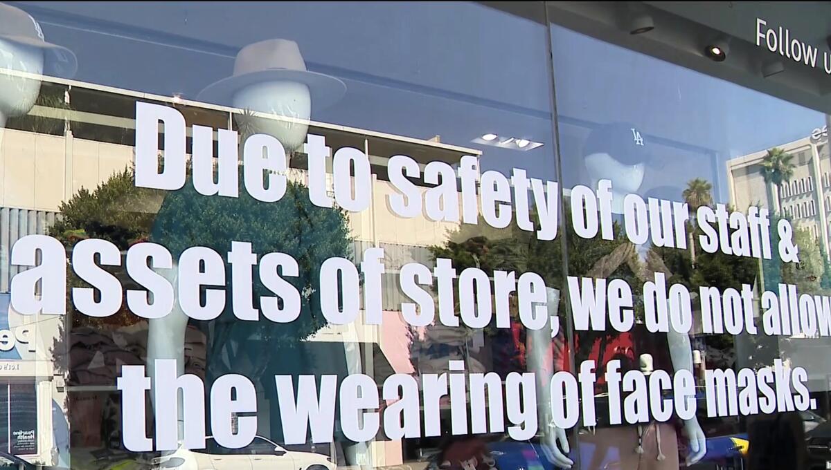 Signage on the front window of Kitson states the store banning masks during its regular business hours