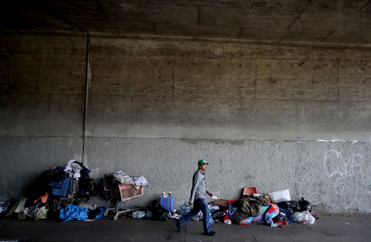 A man walks past a homeless encampment along 9th Street where it cuts under the 110 Freeway in downtown Los Angeles.