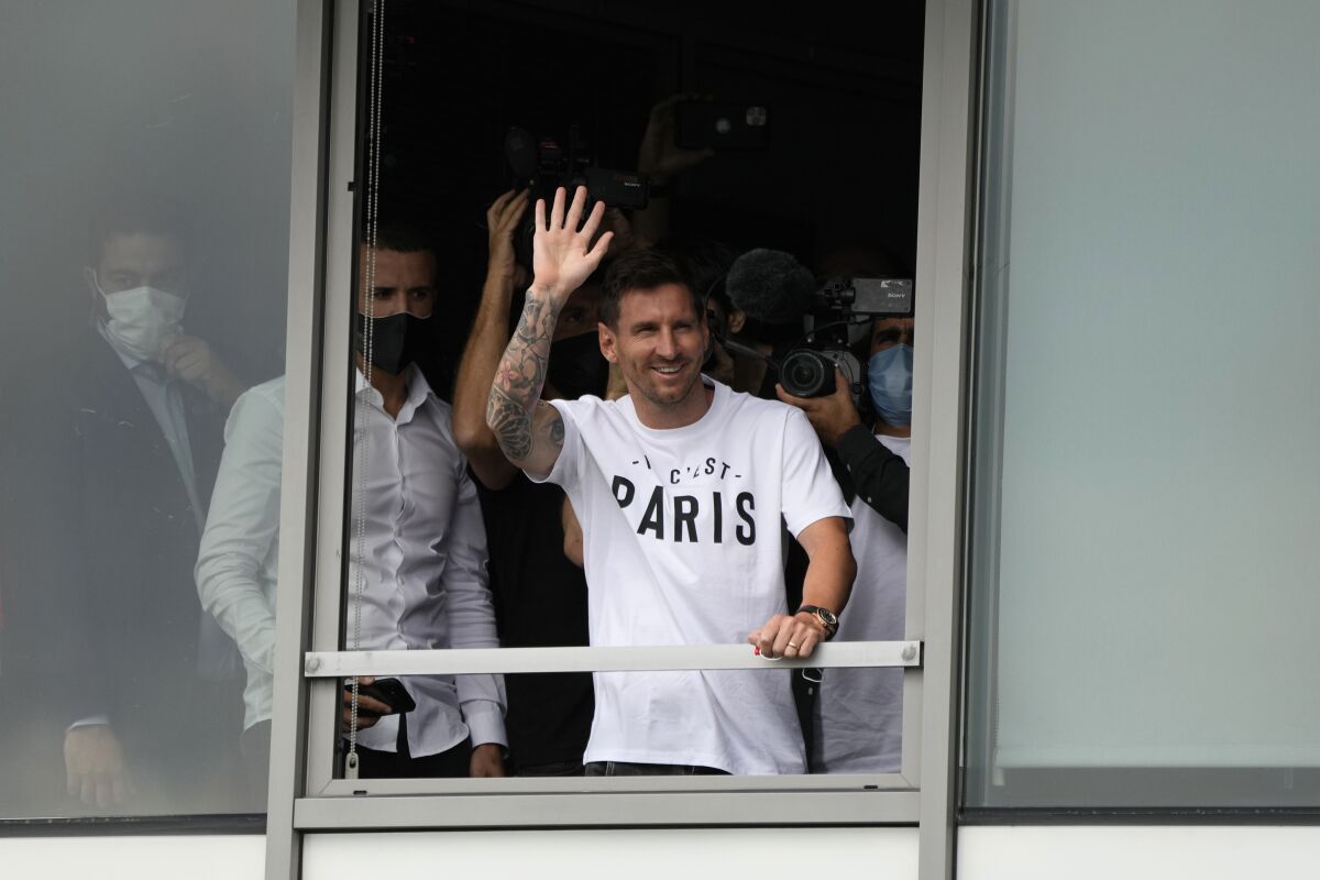 Lionel Messi, wearing a "Paris" shirt, waves out of an airport window.