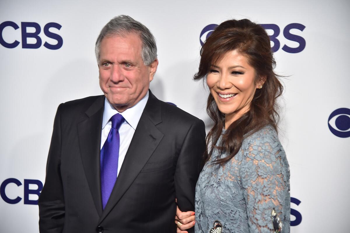 Les Moonves in a dark suit and blue tie poses with Julie Chen, in a lacy gray dress holding onto her husband's arm 