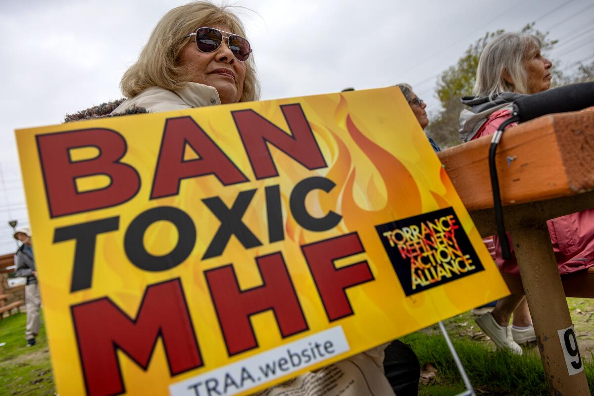 A woman holds a sign that says "Ban toxic MHF."