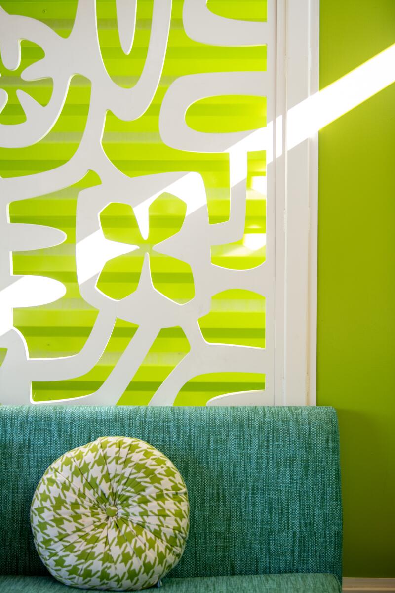 A lime green wall seen through a white patterned cutout, with an aqua sofa with a pillow