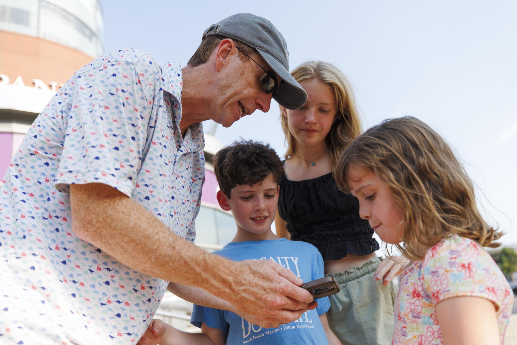 A man leans over and shows his phone screen to three children.