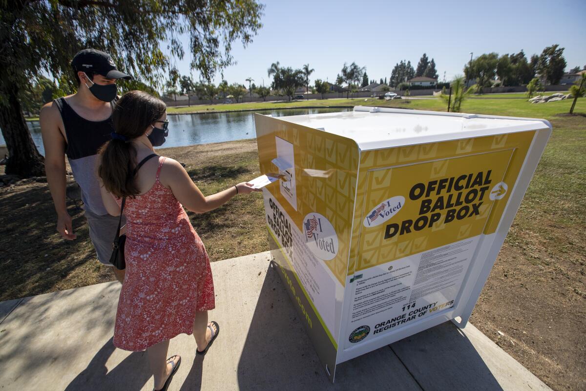 Caitlin Harjes and Angel Santiago place their ballots inside an official Orange County ballot drop box.