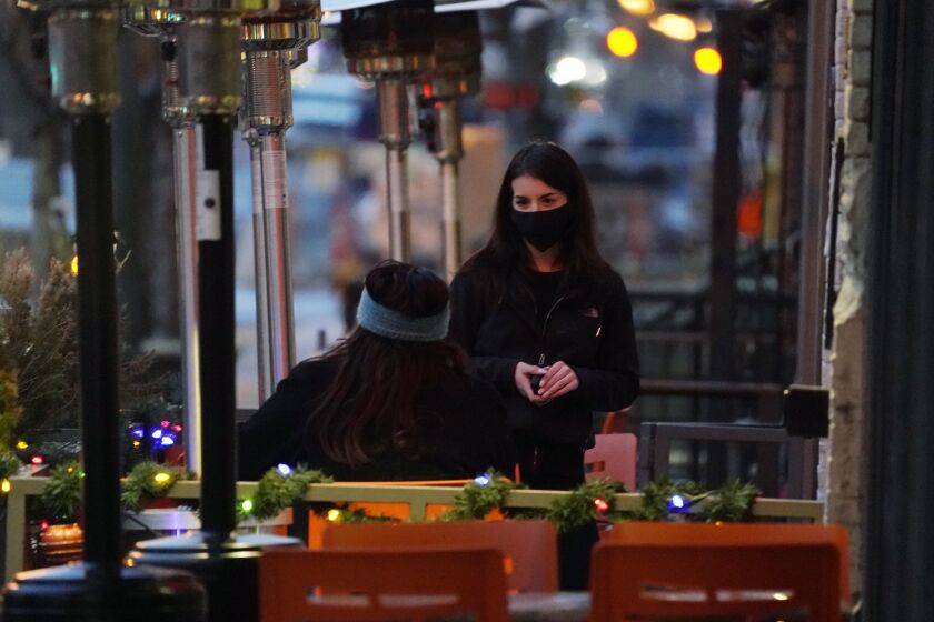 A waitperson wears a face mask while tending to a patron sitting in the outdoor patio of a sushi restaurant, late Monday, Dec. 28, 2020, in downtown Denver. (AP Photo/David Zalubowski)