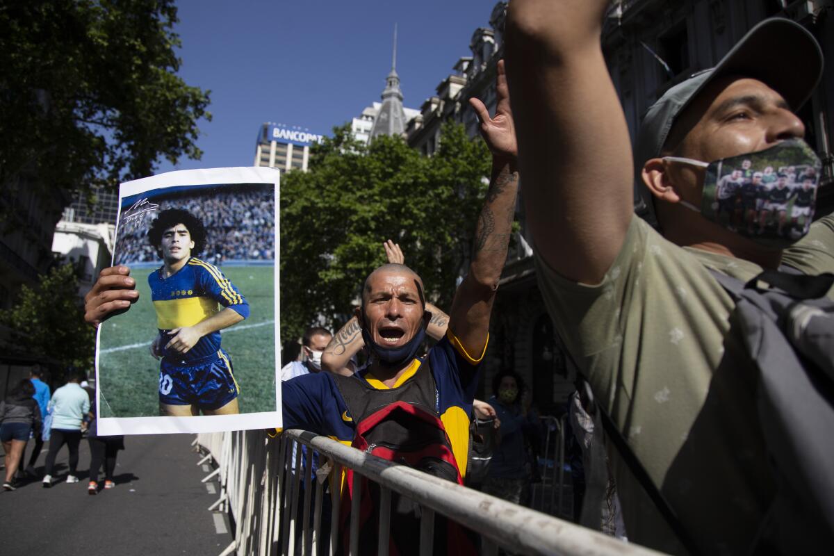 A man stands in a line, arms upraised and holding a picture of young Diego Maradona in his soccer uniform.