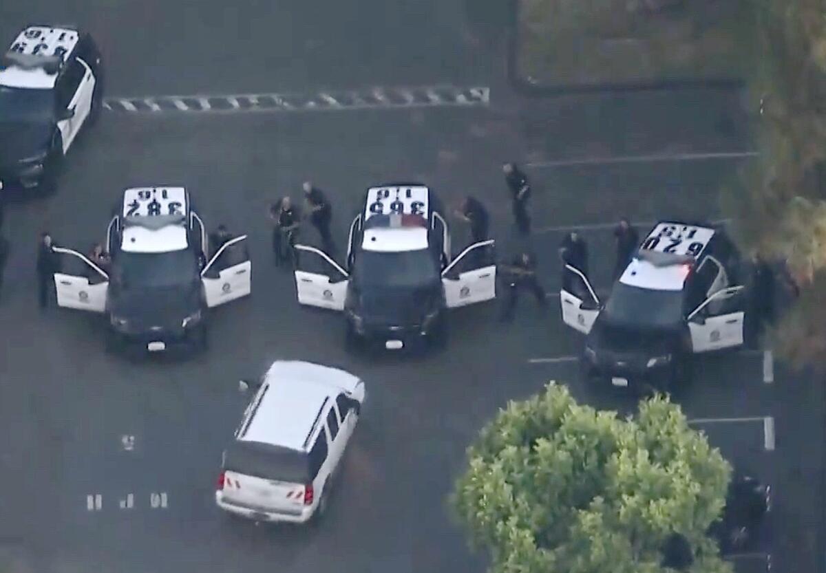 Aerial view of police officers with weapons drawn standing behind the open doors of their cruisers pointing at an SUV