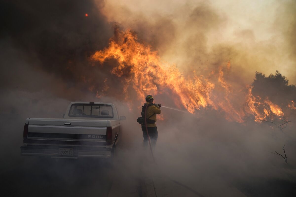 A firefighter next to a Ford truck battles a raging fire amid smoke