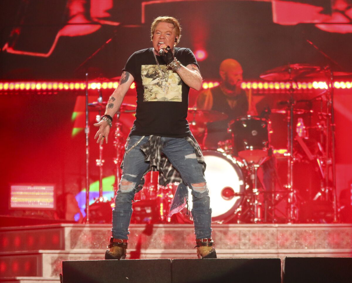 A man with short blond hair wearing a T-shirt and ripped jeans and singing into a microphone on a stage