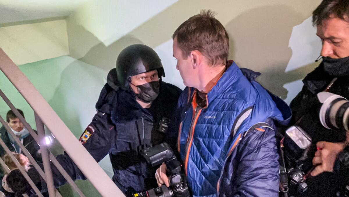 On a stairwell, a helmeted police officer confronts men with cameras.