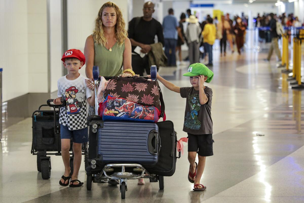 A woman and two children push luggage through an airport terminal.