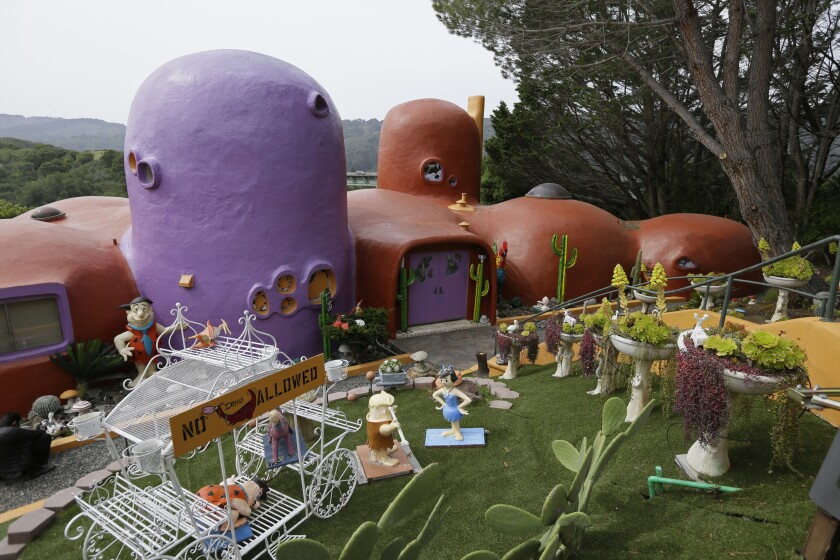 Statues of the Flintstones and other decorations in front of a boulder-like house