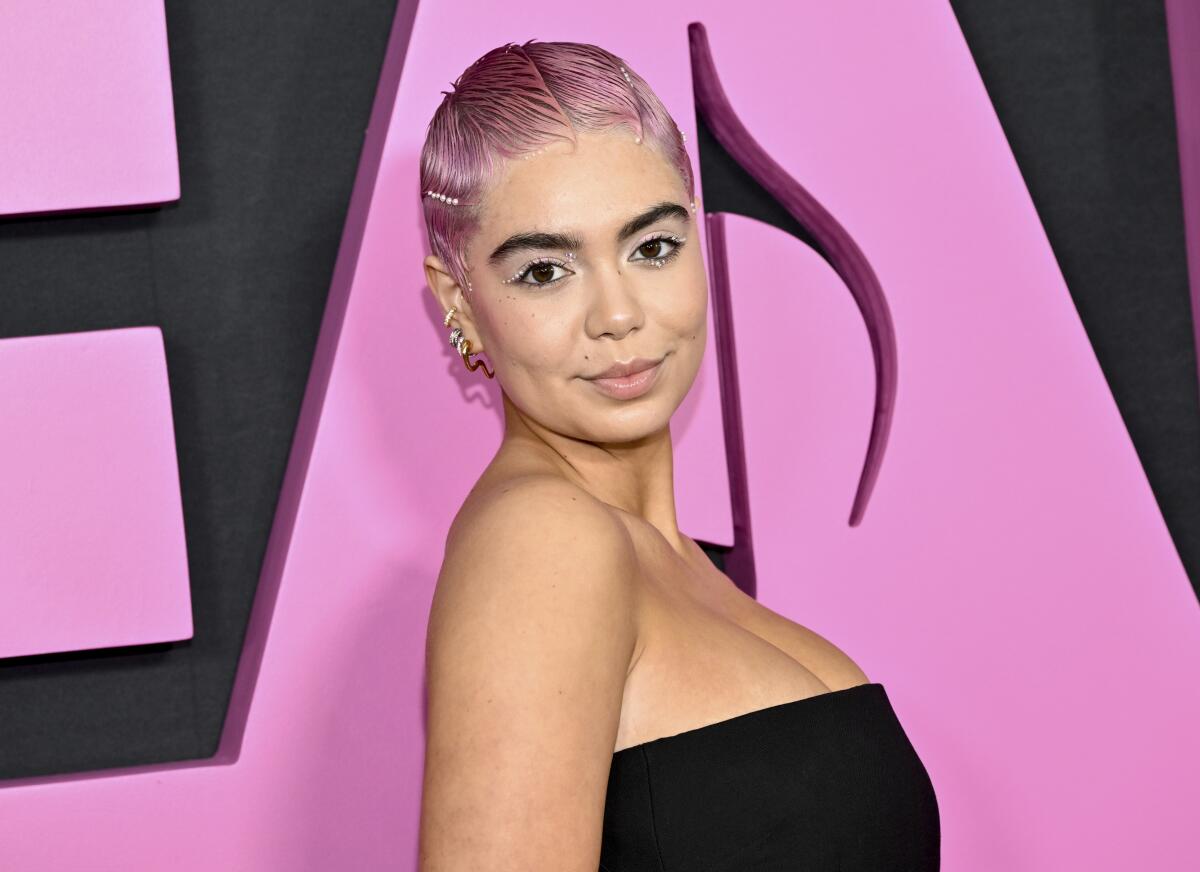 Auli’i Cravalho poses with short pink hair and a black tube-top dress. 