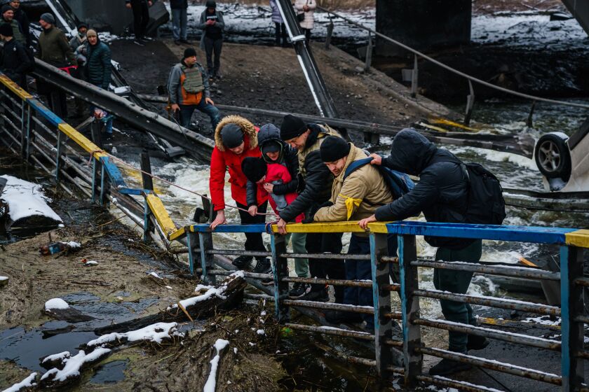 IRPIN, UKRAINE -- MARCH 1, 2022: Soldiers help civilians with their infant child cross a broken bridge over the Irpin river that was destroyed to stop the advancing Russian tanks as they flee their besieged city of Irpin, Ukraine, Tuesday, March 1, 2022. (MARCUS YAM / LOS ANGELES TIMES)