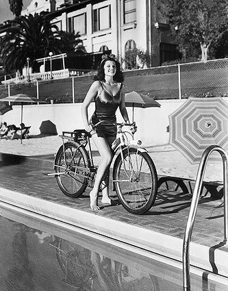 Circa 1940: Rita Hayworth poses poolside on a bicycle.