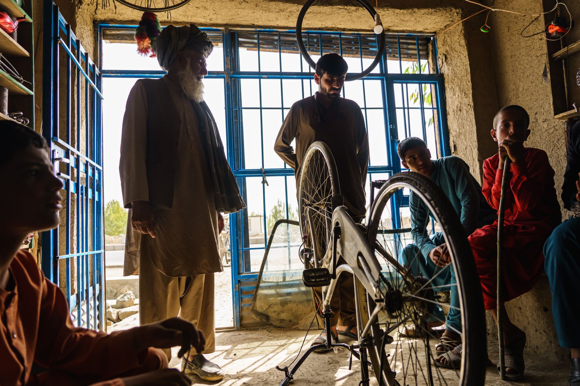 Men sit and stand inside a small shop around an upside-down bicycle.