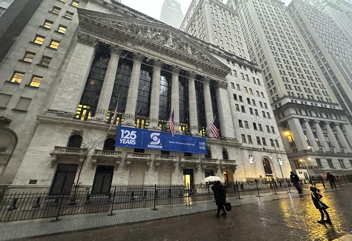 Pedestrians pass the New York Stock Exchange as snow falls.