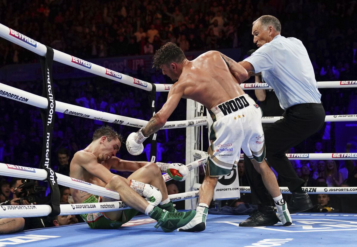 Michael Conlan, left, falls out of the ring after being knocked out by Leigh Wood, center, during their WBA Featherweight World Title fight at the Motorpoint Arena, in Nottingham, England, Saturday, March 12, 2022. (Zac Goodwin/PA via AP)