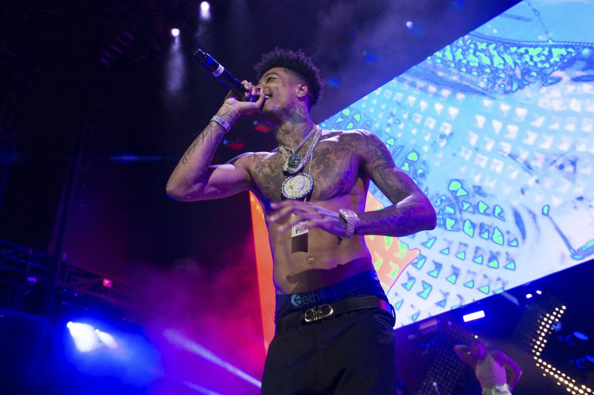 Blueface raps into a microphone while performing shirtless with gold chains around his neck