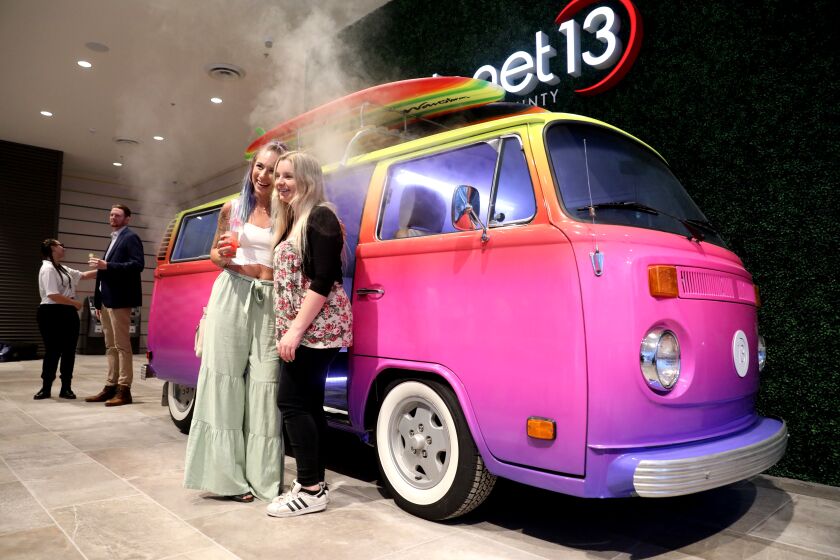 SANTA ANA, CA - JUNE 24: Brianne Puffer, left, of Long Beach, and friend take a photo infant of a restored VW Bus that emits smoke when a button is pushed form inside at a VIP Event at Planet 13, which has an over-the-top superstore dispensary in Las Vegas, is opening what's billed as the "second-largest cannabis superstore in the world" on Thursday, June 24, 2021 in Santa Ana, CA. In addition to employing 250 people and having 50 cash registers, it will have a massive video wall, interactive waves lapping at your feet, a high ceiling covered in multi-colored umbrellas and a 16-foot-tall animatronic octopus. (Gary Coronado / Los Angeles Times)