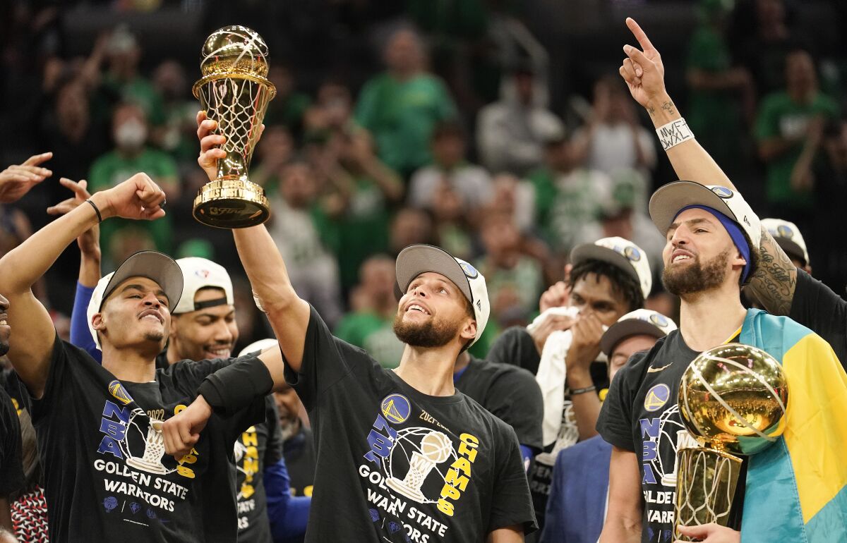 Golden State Warriors guard Stephen Curry, center, holds up the Bill Russell Trophy for most valuable player after the Warriors defeated the Boston Celtics in Game 6 to win basketball's NBA Finals championship, Thursday, June 16, 2022, in Boston. (AP Photo/Steven Senne)
