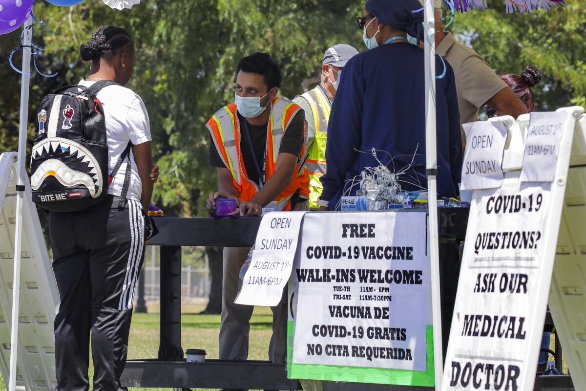 Workers at a tent with signs offering COVID vaccines speak to a person