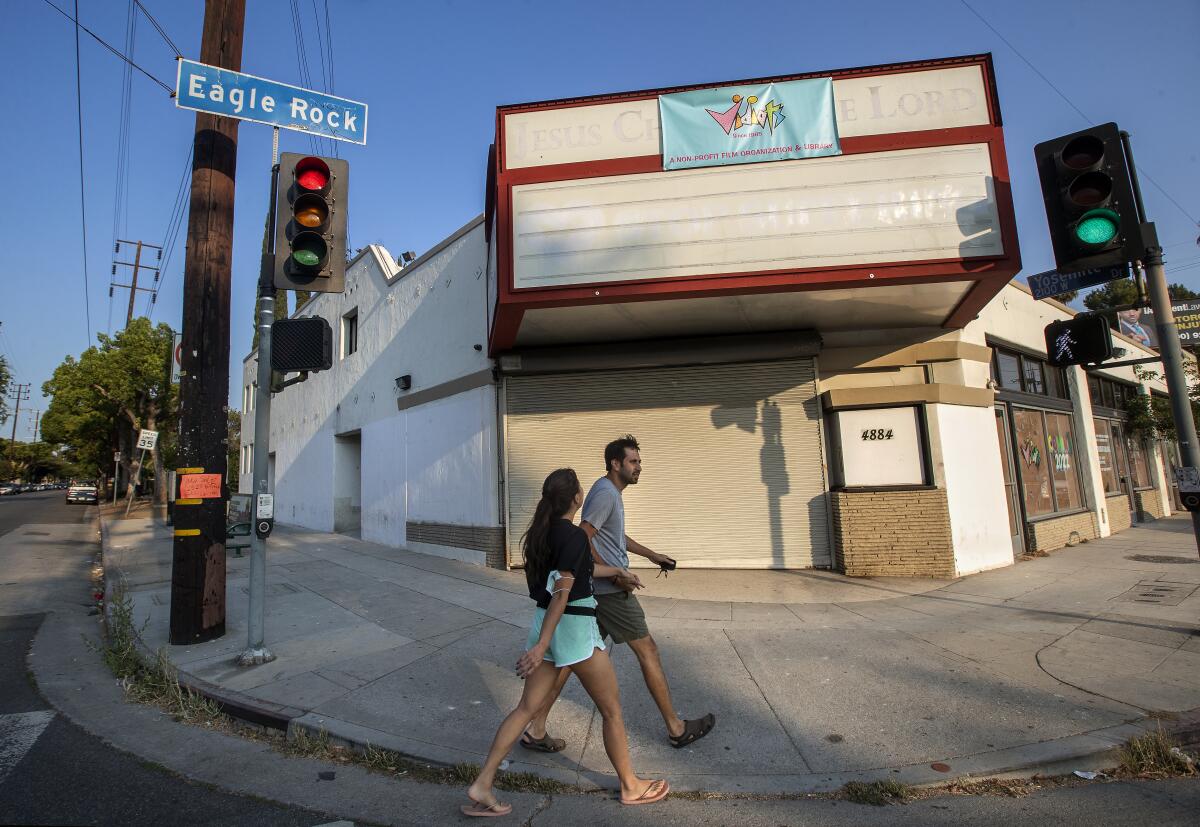 A man and a woman walk under an Eagle Rock street sign and near a building with a blank marquee.