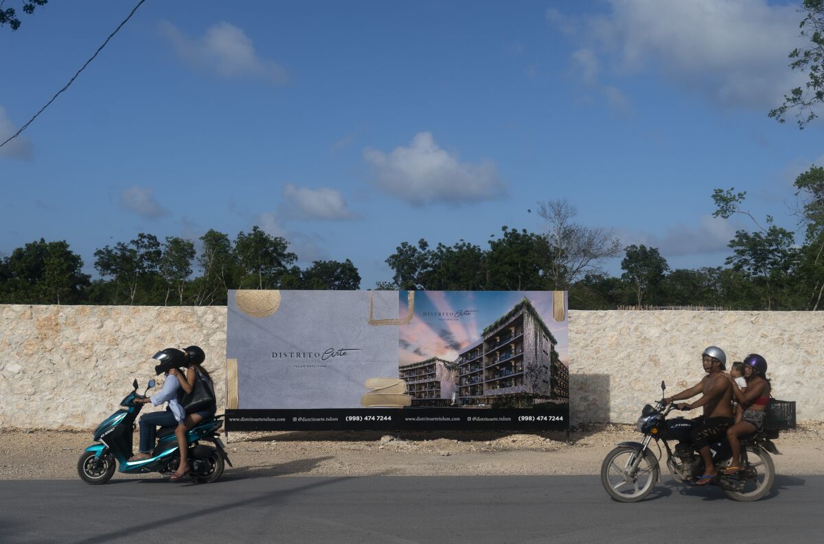 Dos motocicletas pasan frente a un cartel que anuncia la venta de condominios recién construidos en Tulum (México). La mayoría de estos departamentos es comprada por turistas extranjeros. Foto del 4 de agosto del 2022. (AP Photo/Eduardo Verdugo)