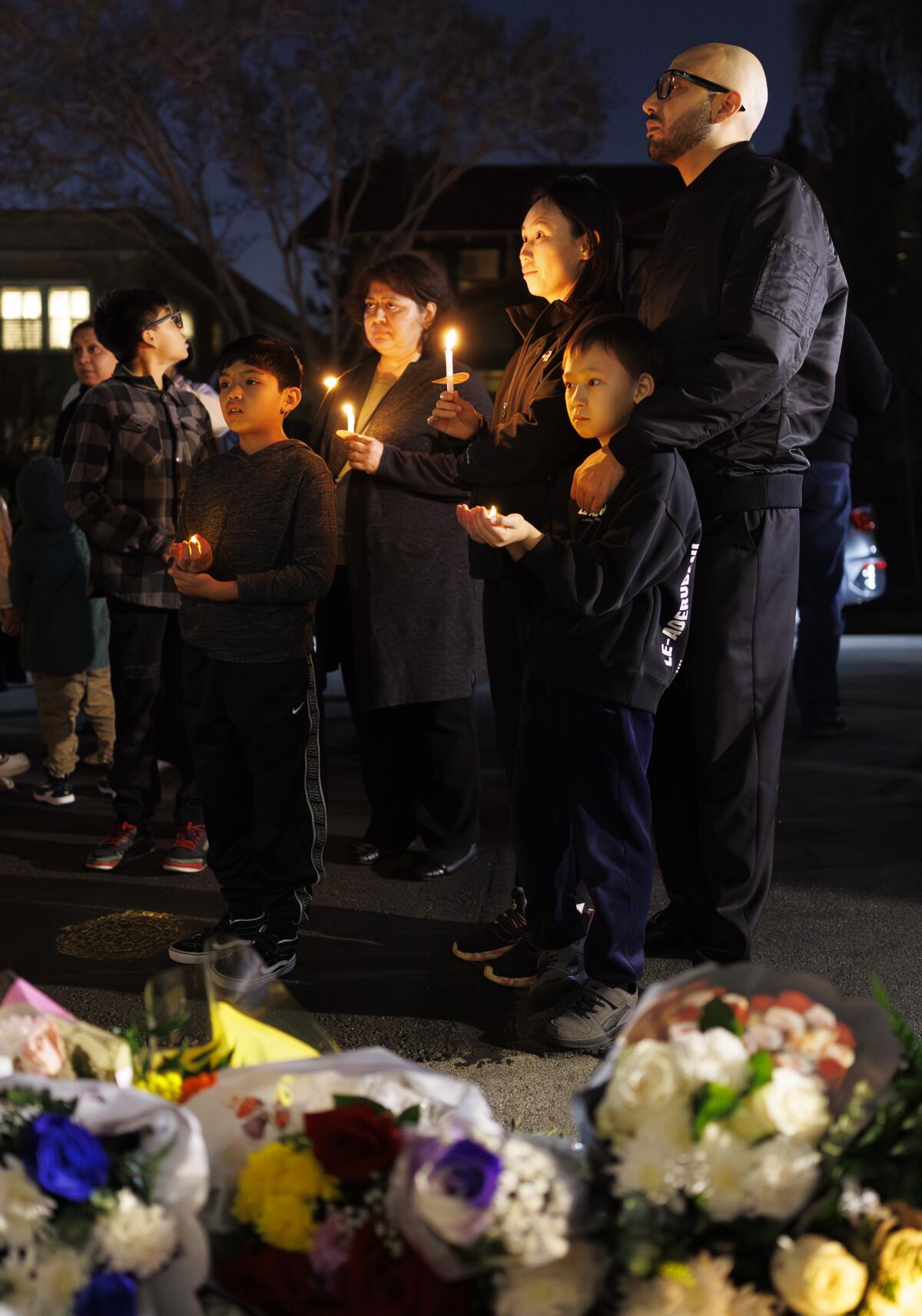People hold candles next to a pile of flowers.