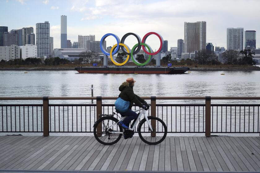 A man rides a bicycle near the Olympic rings floating in the water in the Odaiba section Friday, Jan. 8, 2021 in Tokyo. The senior member of the International Olympic Committee has said he “can’t be certain”the postponed Tokyo Olympics will open in just over six months because of the surging pandemic in Japan and elsewhere. (AP Photo/Eugene Hoshiko)