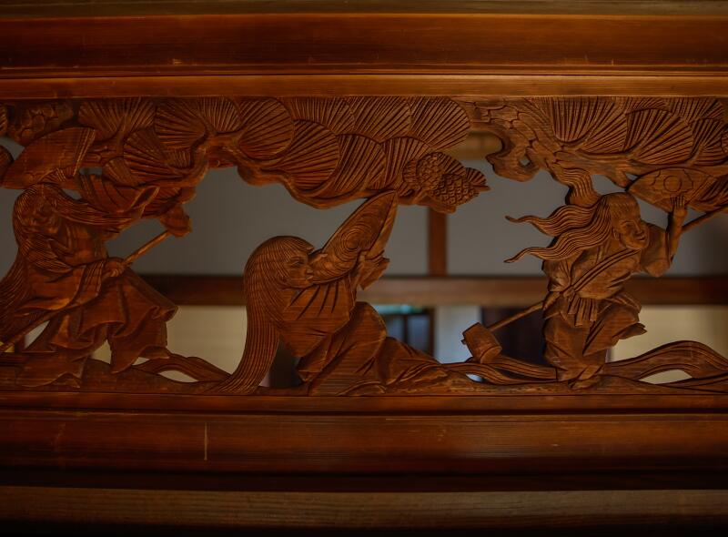 An intricate carving of farm life at the top of the entrance to the shōya house's grand room.