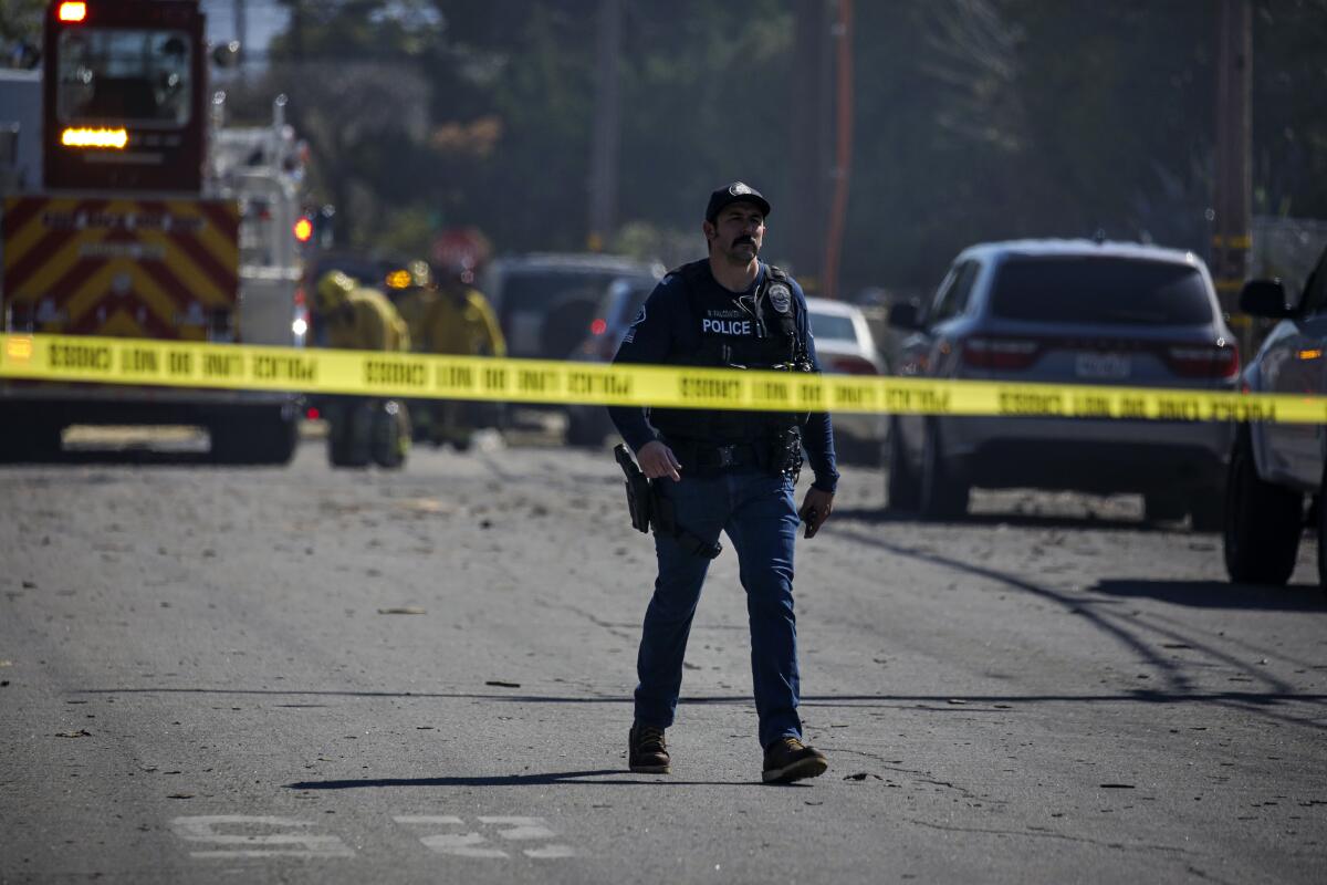 A police officer walks among debris on a street behind yellow police tape