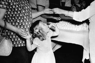 FILE - In this July 18, 1962 file photo, a girl swallows a lump of sugar coated with a dose of the Sabin polio vaccine, served in a paper cup in Atlanta, Ga. Tens of millions of today's older Americans lived through the polio epidemic, their childhood summers dominated by concern about the virus. Some parents banned their kids from public swimming pools and neighborhood playgrounds and avoided large gatherings. Some of those from the polio era are sharing their memories with today's youngsters as a lesson of hope for the battle against COVID-19. Soon after polio vaccines became widely available, U.S. cases and death tolls plummeted to hundreds a year, then dozens in the 1960s, and to U.S. eradication in 1979.(AP Photo/File)