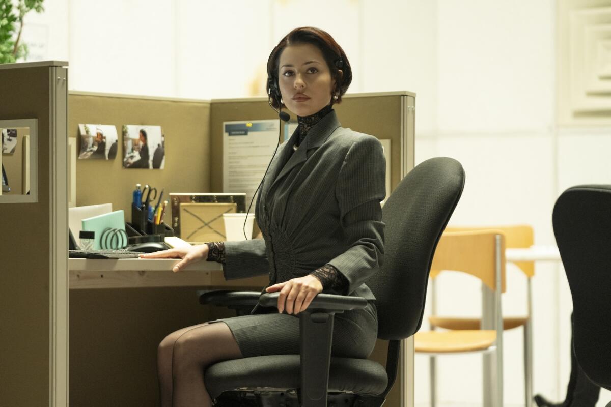 A woman sitting in an office cubicle, wearing a suit and headset.