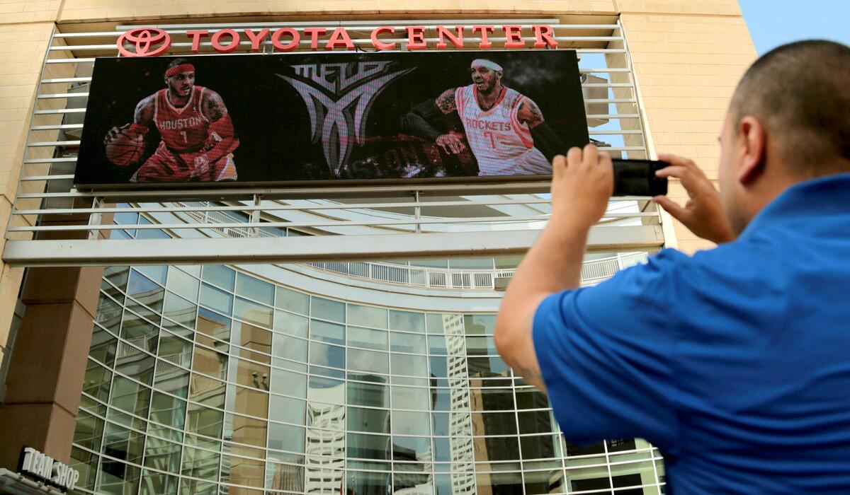 Rockets fan Frank Vasquez takes a photograph of free-agent forward Carmelo Anthony wearing Rockets jerseys in composite images on the Toyota Center videoboard on Wednesday in Houston.