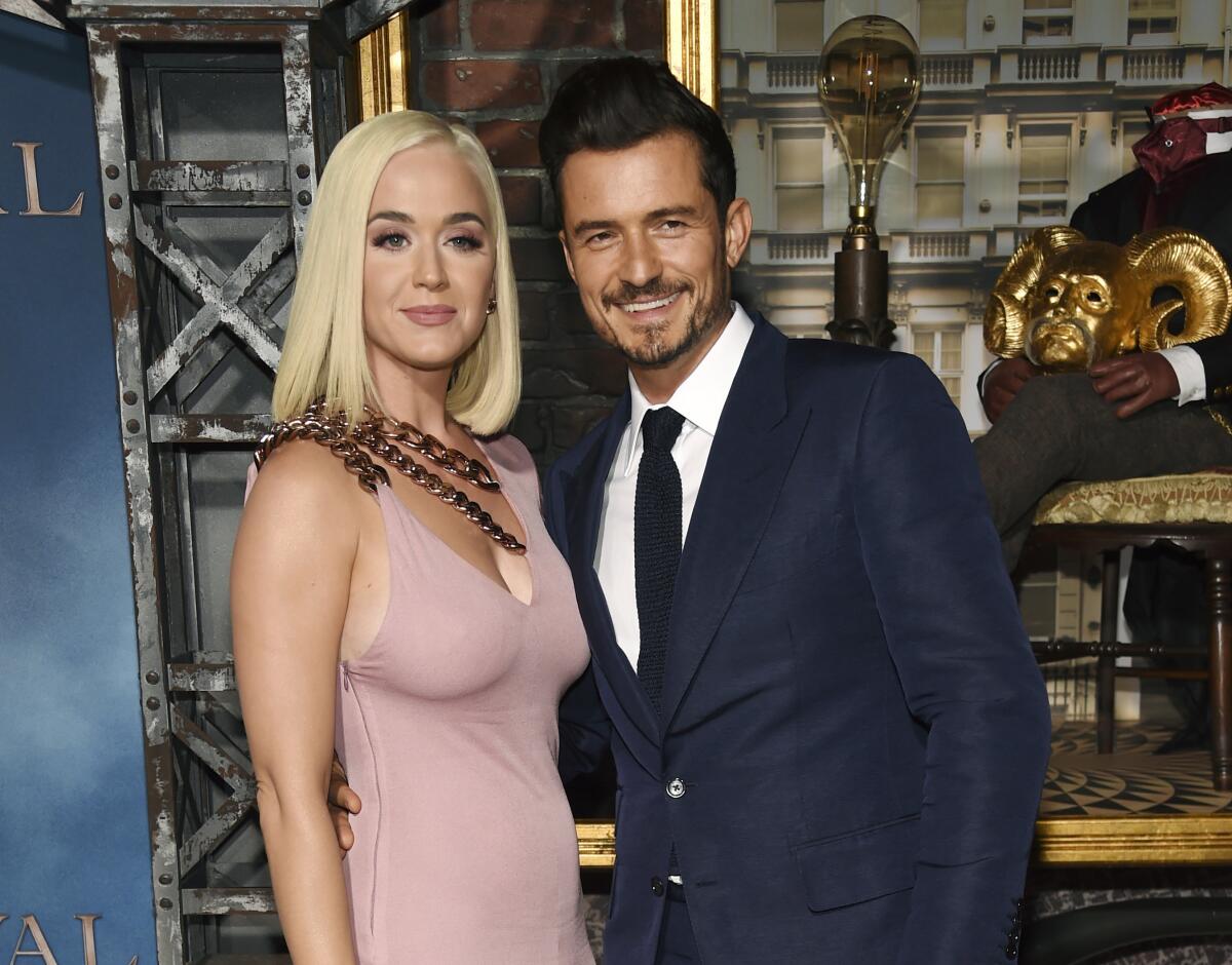 Katy Perry and Orlando Bloom, in a pastel pink dress and dark suit, respectively, pose together.