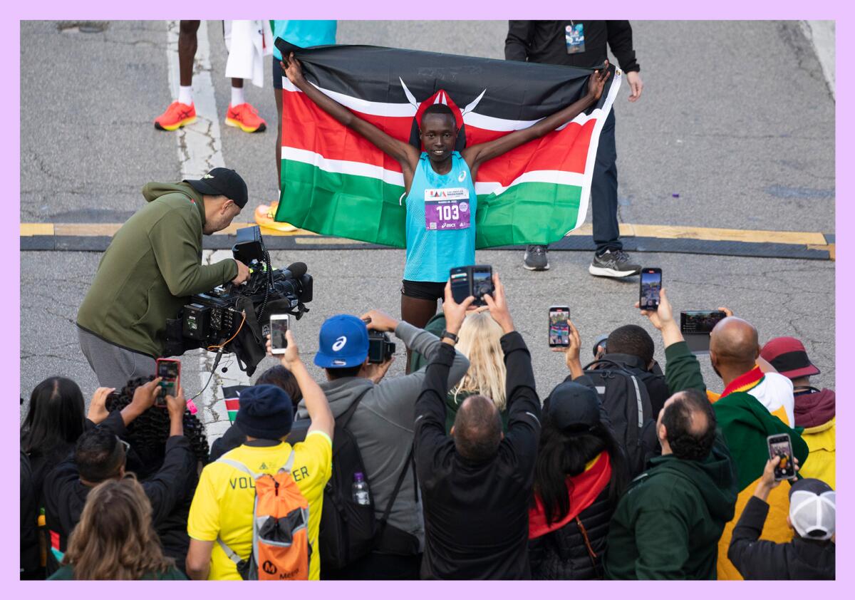 A runner, holding up a Kenyan flag, faces a crowd of people with cameras.