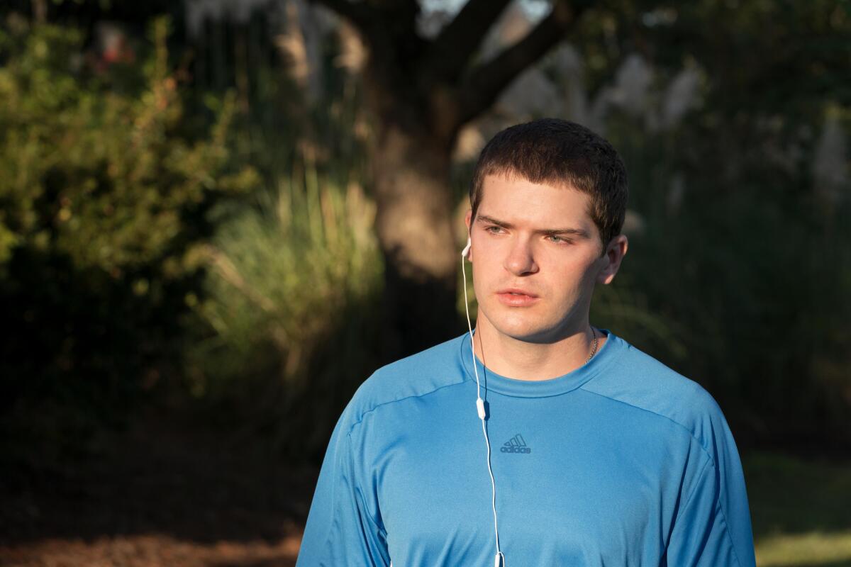 A teenage boy in a blue workout shirt with one white earbud in.