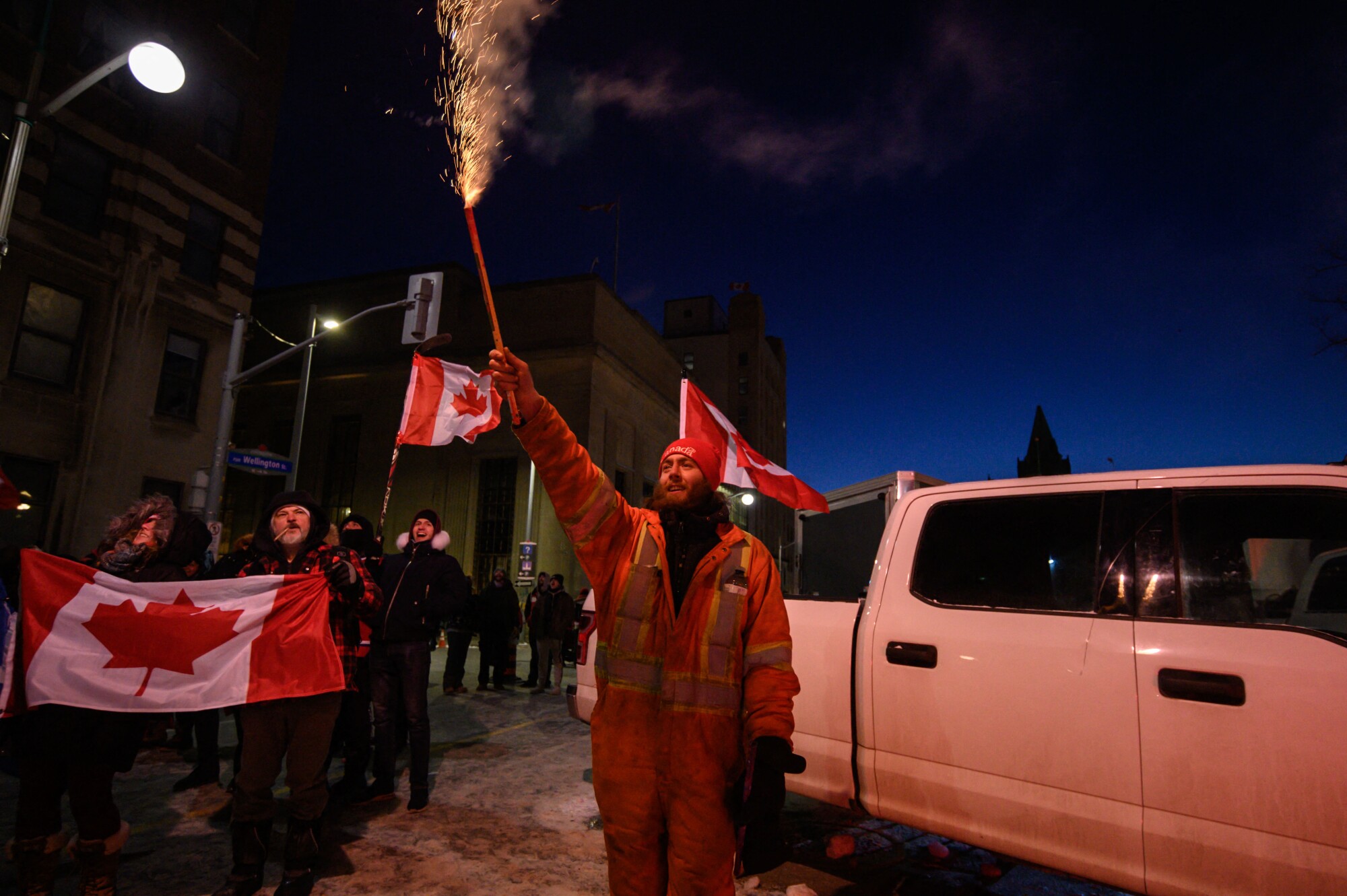 A demonstrator sets off fireworks as Canadian flags wave behind him 